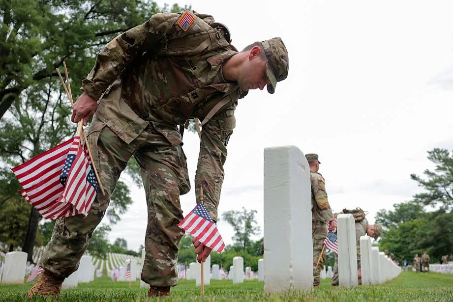 Members of the 3rd U.S. Infantry Regiment place flags in front of each headstone at Arlington National Cemetery on May 21, 2026 in Arlington, Virginia. Before dawn, soldiers begin the process of placing a flag in front of approximately 260,000 headstones ahead of Memorial Day
