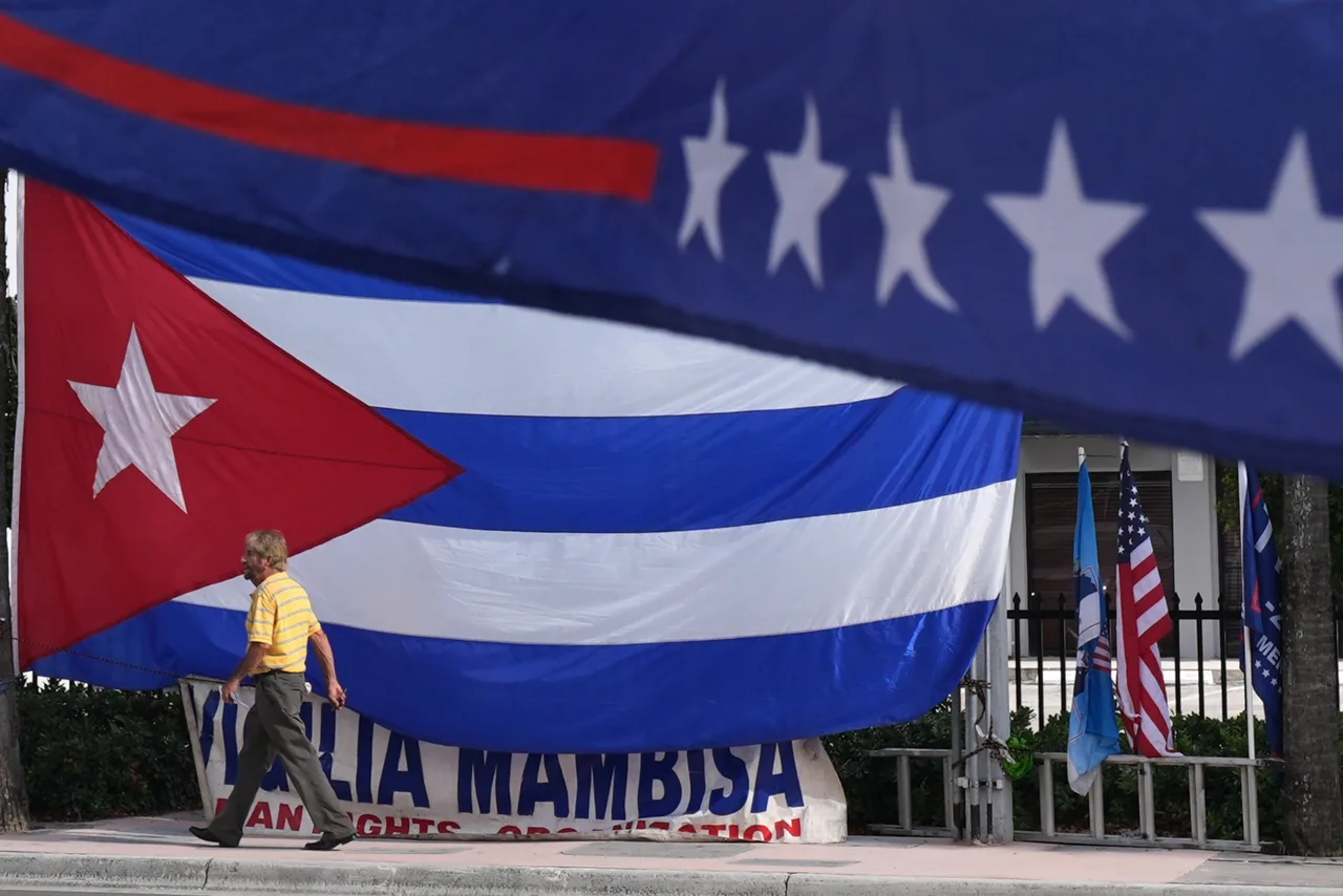 A man walks past a giant Cuban flag as a group of Cubans gathers to hold signs and wave flags hours after federal prosecutors announced charges against former Cuban President Raul Castro